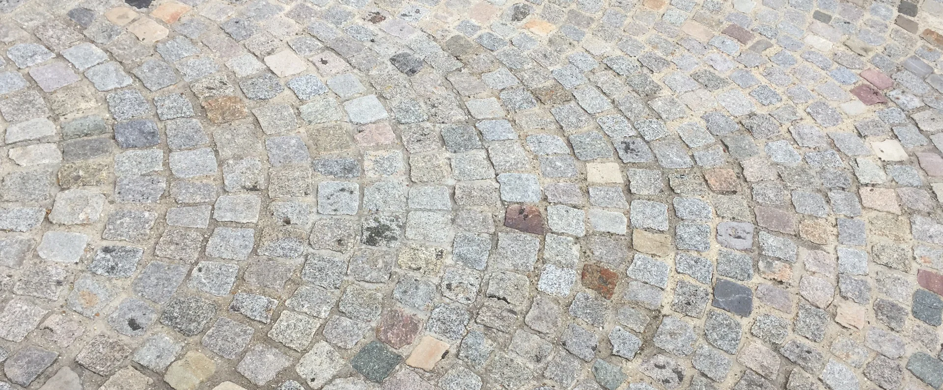 Préparation et lit de pose Kandla pour pavage extérieur. Cette vue de dessus montre les étapes de construction d'une terrasse en pierre naturelle. Une partie des pavés rectangulaires aux nuances ocres, grises et rosées est déjà installée de manière régulière. À côté, la zone sablonneuse et granuleuse préparée met en valeur l'importance d'un lit de pose Kandla soigné. Un maillet de chantier est posé au sol, symbolisant le travail de précision nécessaire pour ajuster chaque pavé et obtenir une surface plane et durable.