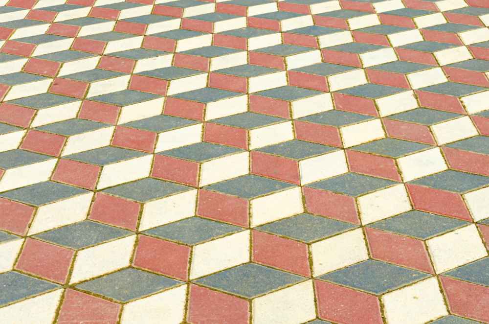 La photographie de l'image Kandla multicolor.jpg montre un revêtement de sol extérieur, probablement une terrasse ou un chemin, réalisé en pavés de grès. La particularité de ce pavement réside dans son motif géométrique en trois dimensions, une illusion d'optique appelée 